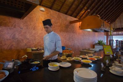 a man in a white shirt and black hat is preparing food on a counter at Vilamendhoo Island Resort & Spa