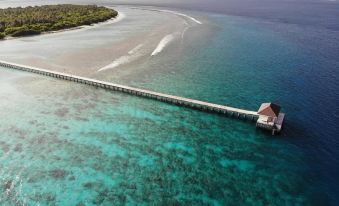aerial view of a long pier extending into the ocean , with a house on the water 's edge at Hondaafushi Island Resort
