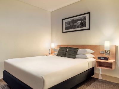 a bed with a white comforter and black and white pillows is shown in a hotel room at Ibis Melbourne Hotel and Apartments