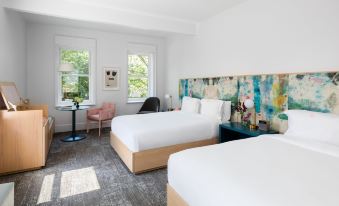 a modern hotel room with two beds , a desk , and large windows , decorated with white bedding and colorful artwork at Quirk Hotel Charlottesville