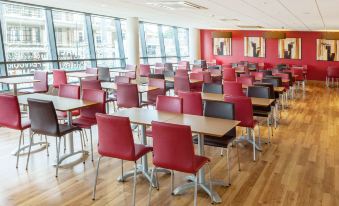 a large dining area with wooden tables and chairs , red chairs , and a wooden floor at Travelodge Slough