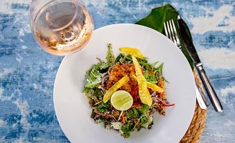 a white plate with a salad and a glass of wine on a blue table at Turtle Bay Lodge