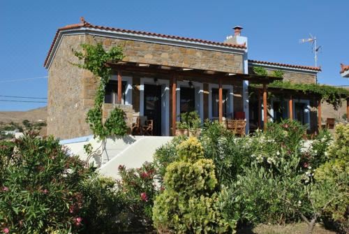 a stone house surrounded by a lush garden , with various plants and flowers blooming in the yard at Victoria Limnos