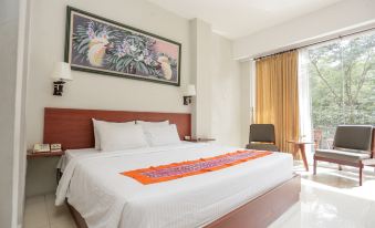 a large bed with a white comforter and orange runner in a room with a window and curtains at Ubud Hotel & Cottages