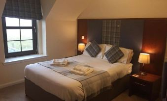 a neatly made bed with white sheets and a plaid blanket is situated in a room with two lamps at Polochar Inn