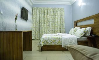 a modern bedroom with wooden furniture , white bedding , and a green floral patterned curtain , along with a tv on the wall at Hotel Lewi