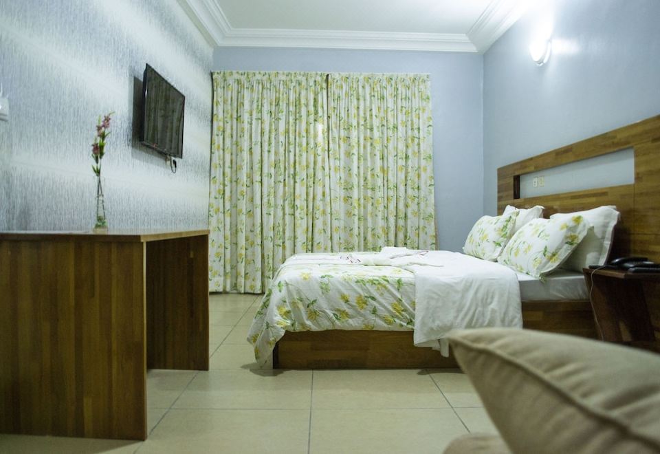 a modern bedroom with wooden furniture , white bedding , and a green floral patterned curtain , along with a tv on the wall at Hotel Lewi