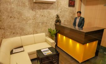 a man standing behind a reception desk in a hotel lobby , with a couch and a coffee table in the background at Emporio Hotel