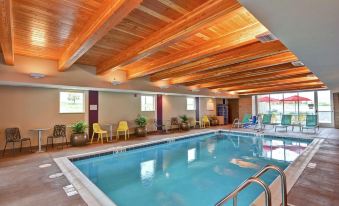 an indoor swimming pool with a wooden ceiling , surrounded by chairs and tables , in a well - lit room at Home2 Suites by Hilton Helena