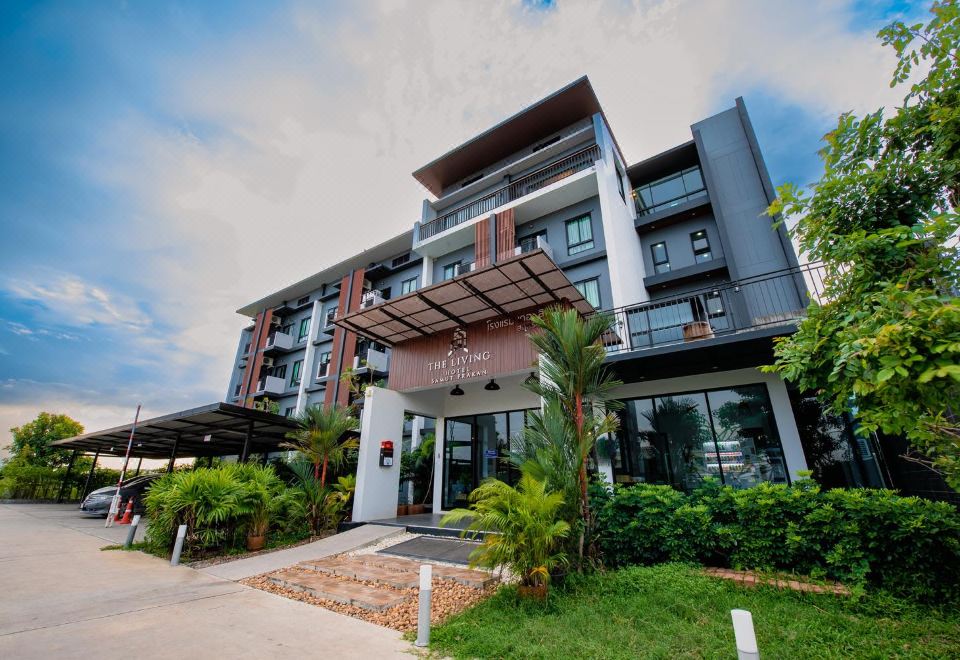 a modern , multi - story apartment building with a large parking garage in the front , surrounded by greenery at The Living Hotel SamutPrakan