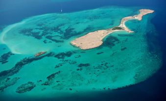 an aerial view of a small island surrounded by clear blue water with a white sailboat in the distance at Djibouti Palace Kempinski