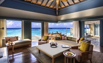 a spacious living room with a couch , chairs , and a dining table in front of a window overlooking the ocean at Raffles Maldives Meradhoo Resort