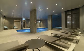 a modern indoor pool area with several lounge chairs and tables , surrounded by a building at Hotel Princess