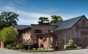 a brick building with a wagon parked in front and trees surrounding the area , under a clear blue sky at Bredbury Hall Hotel