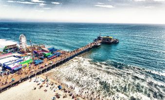 a crowded beach scene with a pier and boats , set against the backdrop of a cloudy sky at Hotel Carmel Santa Monica