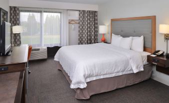 a large bed with white linens and a headboard is in a room with a window at Hampton Inn Portland East