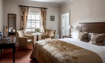 a bedroom with a bed , two chairs , and a window with curtains , all in white at Chilston Park Hotel