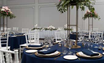 a large dining room with several round tables covered in blue tablecloths , surrounded by white chairs at Rydges Southbank Townsville, an EVT hotel