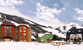 a snowy mountain scene with a building in the foreground and a green building in the background at Village Condo