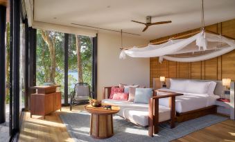 a modern bedroom with wooden furniture , white bedding , and a large window offering views of the outdoors at Six Senses Krabey Island