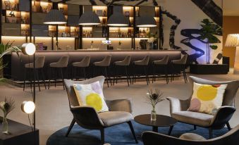 a modern lounge area with a bar and several chairs , creating a comfortable and inviting atmosphere at Mercure Geneva Airport