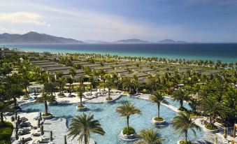 a resort with a large pool surrounded by palm trees and a view of the ocean at Movenpick Resort Cam Ranh