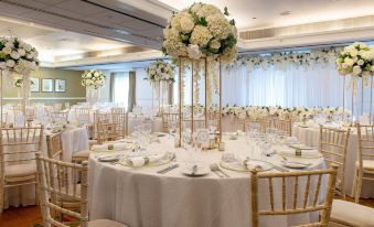 a large dining room with multiple tables covered in white tablecloths and adorned with tall white centerpieces at Delta Hotels Tudor Park Country Club