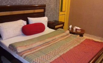 a bed with a red and white pillow , a nightstand with a lamp , and a colorful quilt at Royal Inn