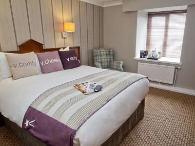 a neatly made bed with a striped blanket and purple pillows is shown in a hotel room at Village Hotel Liverpool