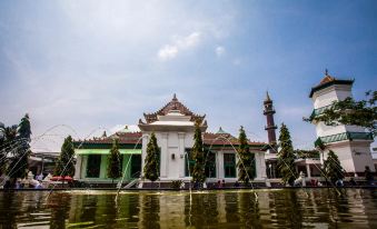 a large white building with a green roof is surrounded by water and has a tall tower in the background at RedDoorz Plus Near Uin Raden Fatah Palembang