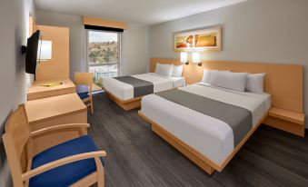a modern hotel room with two beds , a desk , and a window offering a view of the city at City Express by Marriott Nogales