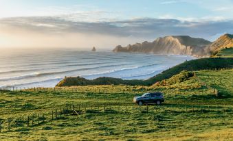 a black car is parked on a grassy hillside overlooking the ocean , with a fence and rocks in the background at Rosewood Cape Kidnappers