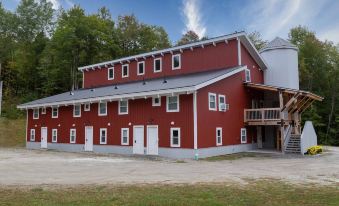 a large red building with multiple windows and a gray roof , situated in a grassy field at Mad River Lodge