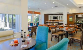 a modern restaurant with wooden tables and chairs , orange tablecloths , and a blue chair in the center at Hilton Garden Inn Nanuet