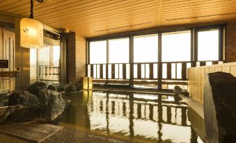 a large indoor hot tub filled with water , surrounded by wooden benches and a view of the outdoors at Dormy Inn Mishima