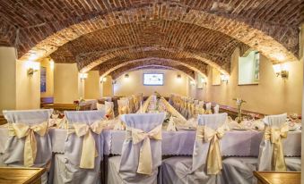 a room with brick walls and a vaulted ceiling has rows of tables covered in purple tablecloths and chairs at Hotel Europa