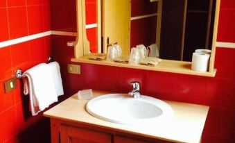 a bathroom sink with a white basin and wooden cabinet , set against a red wall at Hotel Aurora