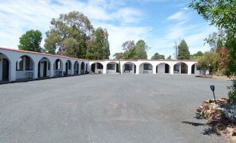 a large , empty parking lot with white walls and arches , surrounded by trees and under a blue sky at Azalea Motel