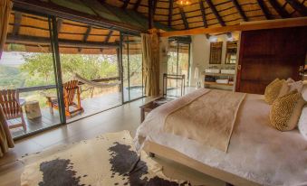 a large bed with a cowhide rug in the middle of a room with a view of trees at Leopard Mountain Safari Lodge