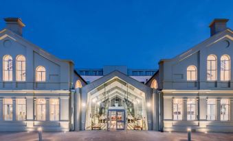 a modern building with a glass entrance and a blue sky in the background , lit up at night at Titanic Hotel Belfast