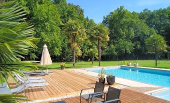 a large wooden deck with chairs and umbrellas overlooks a pool surrounded by lush green trees at Chateau Saint Martin B&B