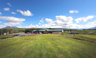 a large grassy field with a few cars parked on the side , and a building in the background at Hotel Eyjafjallajokull