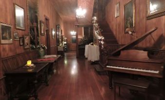 a long , dimly lit hallway with wooden floors and chandeliers , featuring a piano and a dining table in the center at Blythewood Plantation