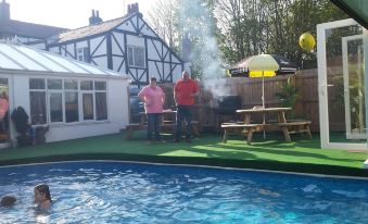 a group of people standing around a pool , enjoying the hot summer day with smoke coming out of the chimney at Tudor House