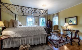 a cozy bedroom with a four - poster bed , a rug on the floor , and a chair near the window at Hillcrest Mansion Inn