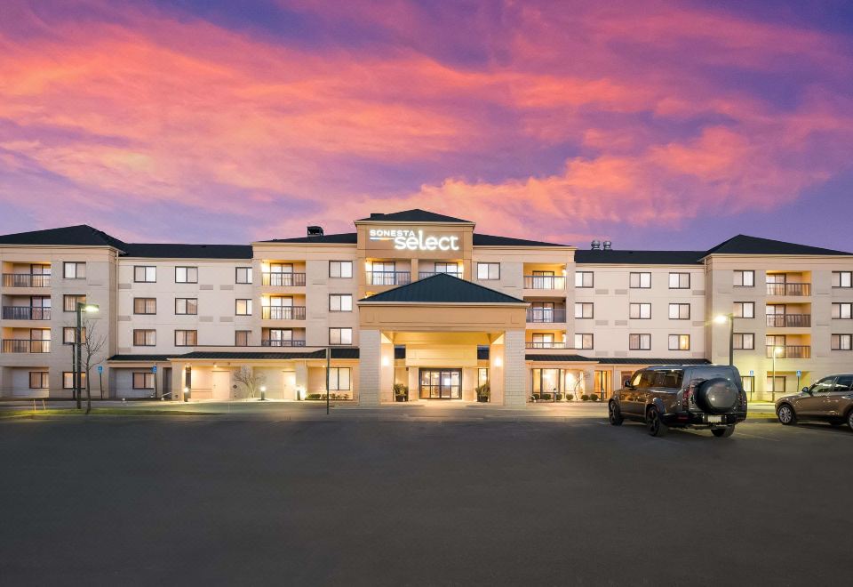 "a large hotel building with a sign that says "" the select "" is illuminated at sunset" at Sonesta Select Detroit Novi