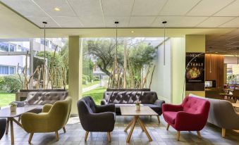 a modern living room with colorful chairs and couches arranged around a coffee table , creating a cozy atmosphere at Novotel Paris Nord Expo Aulnay