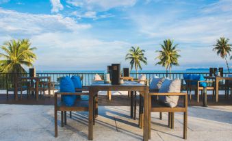 a wooden dining table surrounded by blue pillows on a patio overlooking the ocean , with a laptop placed on the table at Seanery Beach Resort