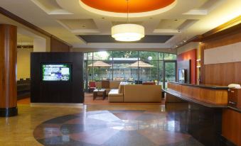a modern hotel lobby with a large circular light fixture , comfortable seating , and an array of dining tables and chairs at Courtyard by Marriott Boston Brookline