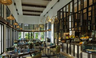 a modern restaurant with a long dining table , chairs , and a buffet filled with various food items at Pullman Maldives All-Inclusive Resort